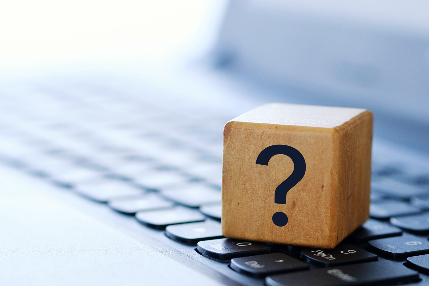A wooden block printed with a question mark, resting on a laptop keyboard